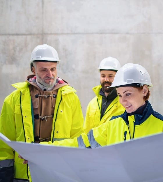 Construction workers in safety gear reviewing plans at a concrete site.