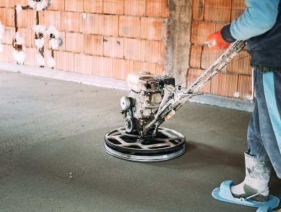 Concrete floor being smoothed with a power trowel at construction site.