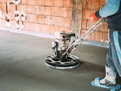 Concrete floor being smoothed with a power trowel at construction site.